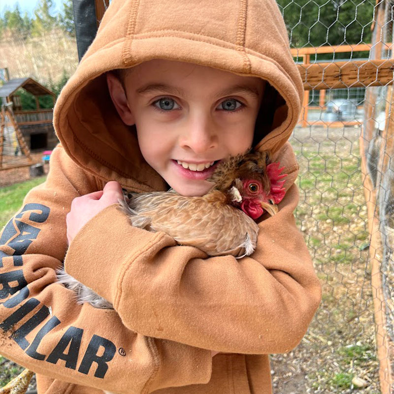 little boy with a hoodie hugging a small chicken