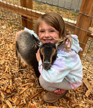 little girl smiling and hugging a baby goat